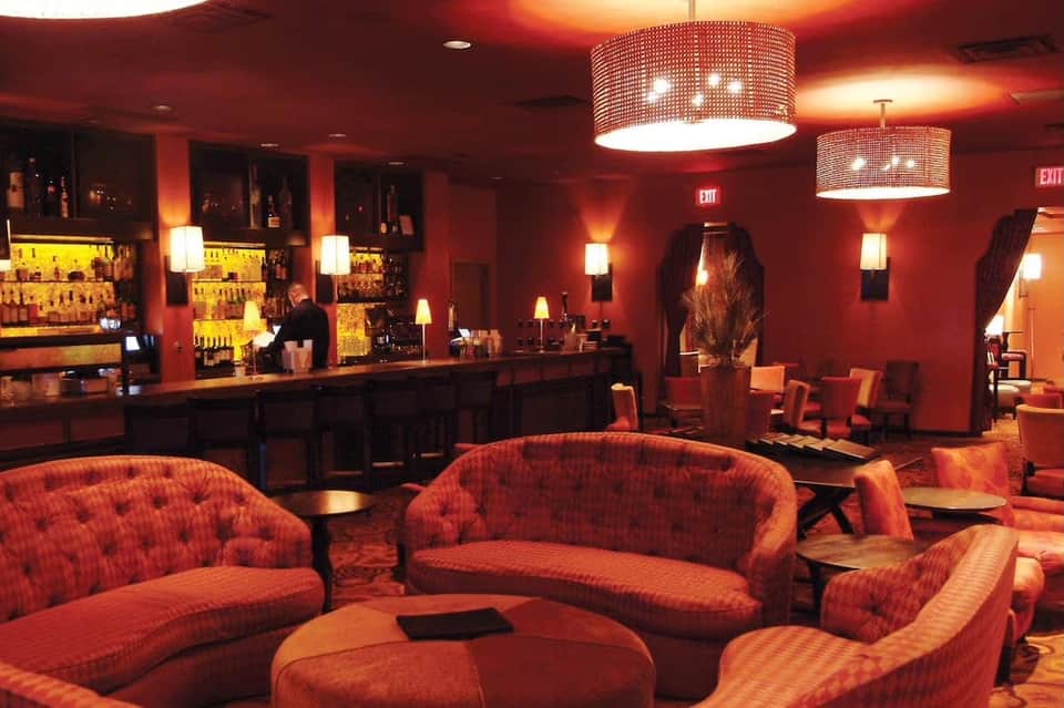 Upscale hotel bar with red ambient lighting, curved seating, and illuminated liquor shelves