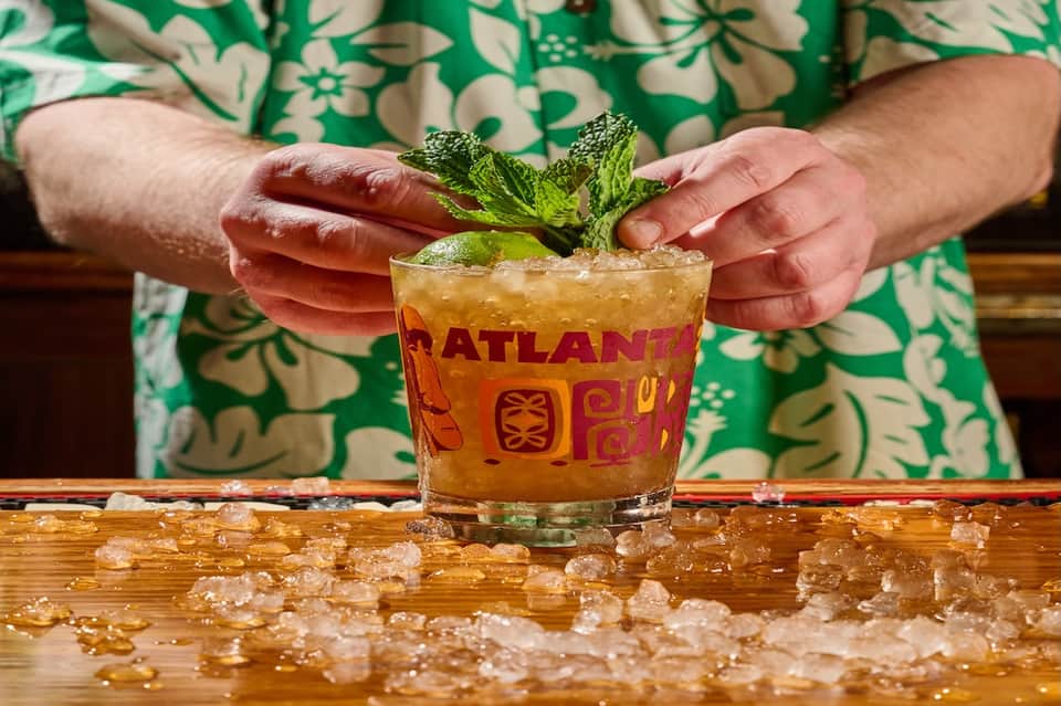 Tropical cocktail with mint garnish being served in branded glass with ice on wooden counter