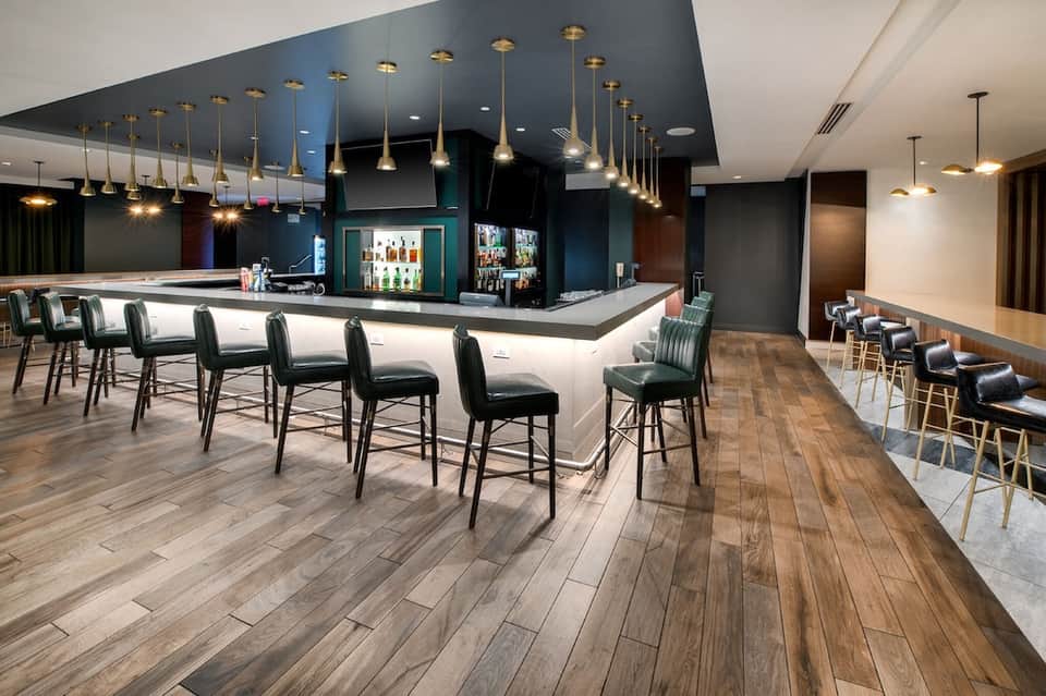 Modern hotel bar lounge with dark blue ceiling, brass pendant lights, white bar counter, and seating area