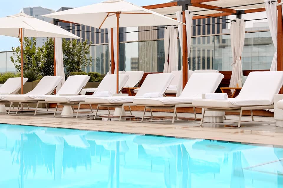 Resort pool deck with white loungers, umbrellas, pergolas, and high-rise buildings in background