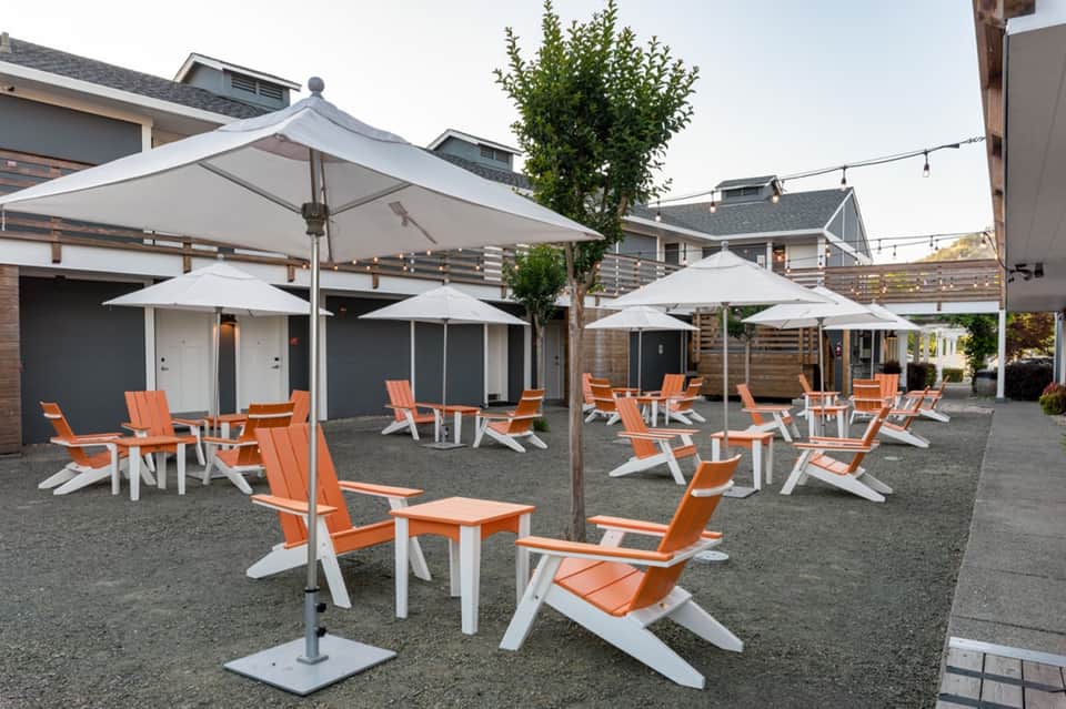 Outdoor patio with orange and white Adirondack chairs arranged under white umbrellas near residential homes