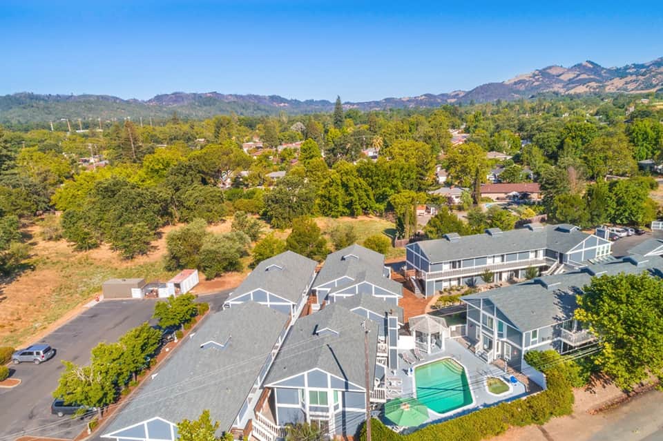 Aerial view of residential homes with swimming pool surrounded by trees and mountains in background