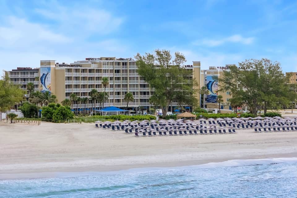 Beachfront hotel with multi-story tan building, blue and white striped umbrellas, and ocean view
