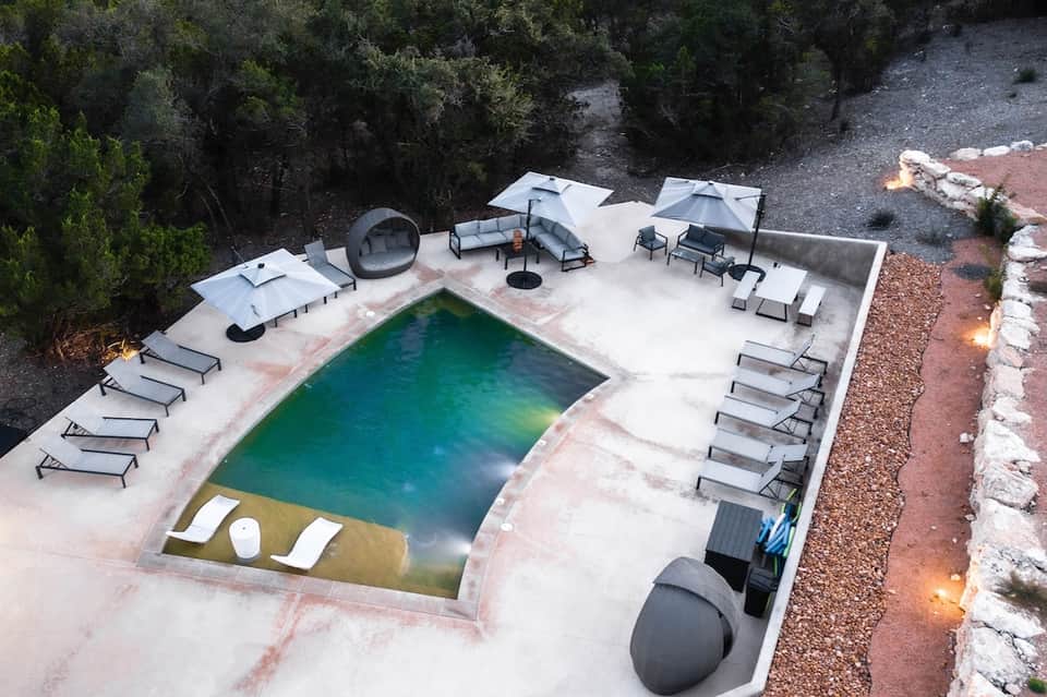 Aerial view of small resort pool surrounded by loungers, umbrellas, fire pits, and natural rocky landscape