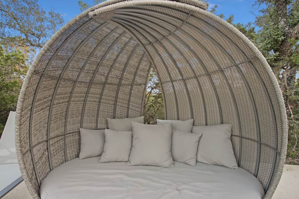 Woven rattan pod-shaped outdoor seating with curved dome, beige cushions, set in landscaped garden