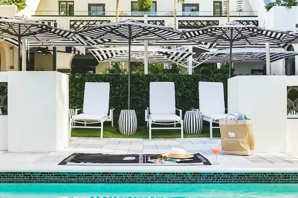 Luxury pool deck with lounge chairs, pergola shade structure, white privacy screens, and teal pool edge