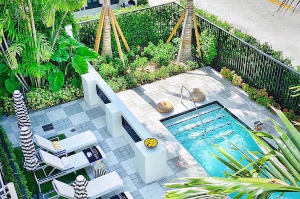 Aerial view of compact luxury pool with white loungers, tropical plants, and waterfront view