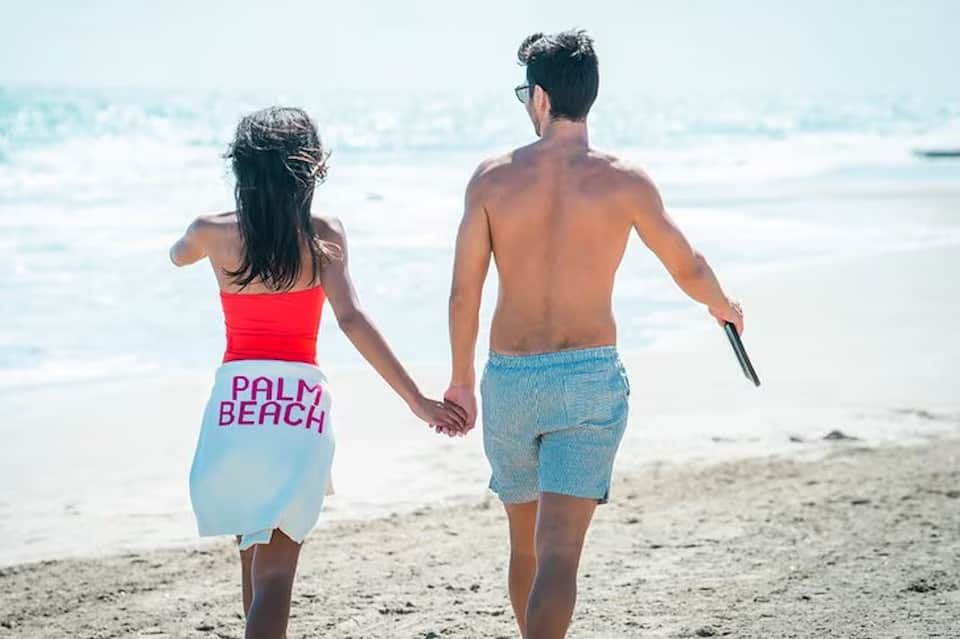 Couple holding hands running toward ocean at sunset beach with sandy shore and calm waters