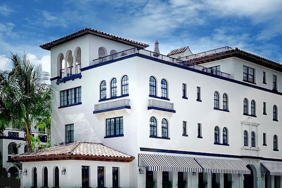 Spanish Colonial-style hotel exterior with white walls, blue balconies, arched windows, and palm tree