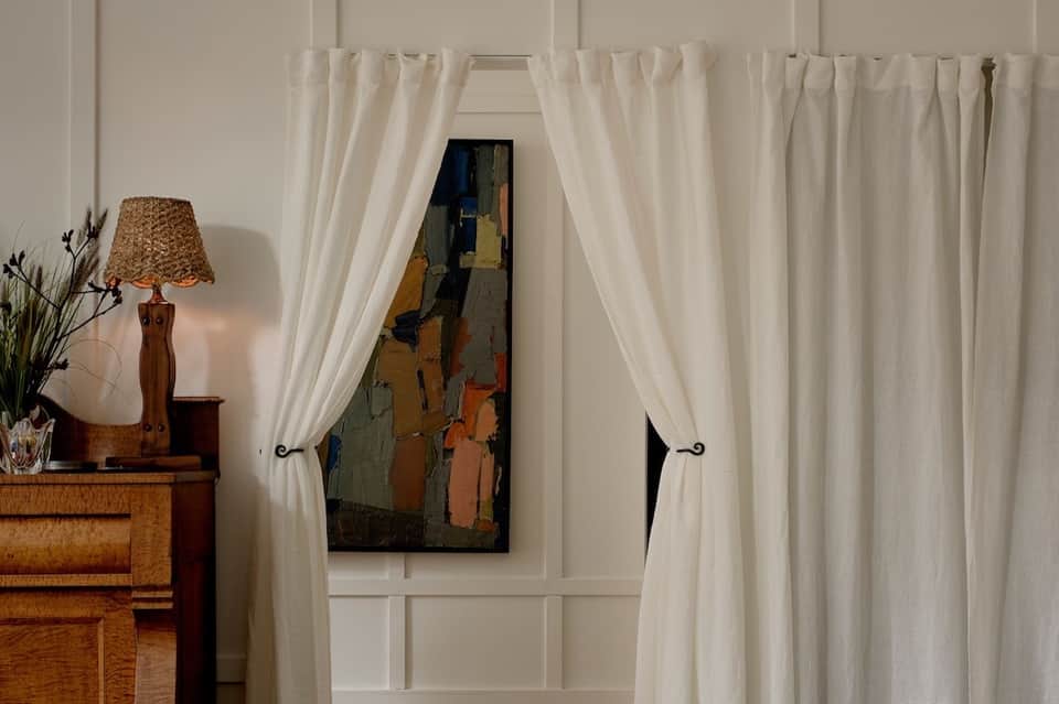Elegant entryway with cream curtains framing doorway and wooden side table with lamp