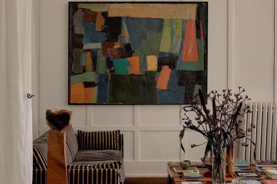 Living room with striped accent chair, abstract artwork, and botanical arrangement on side table