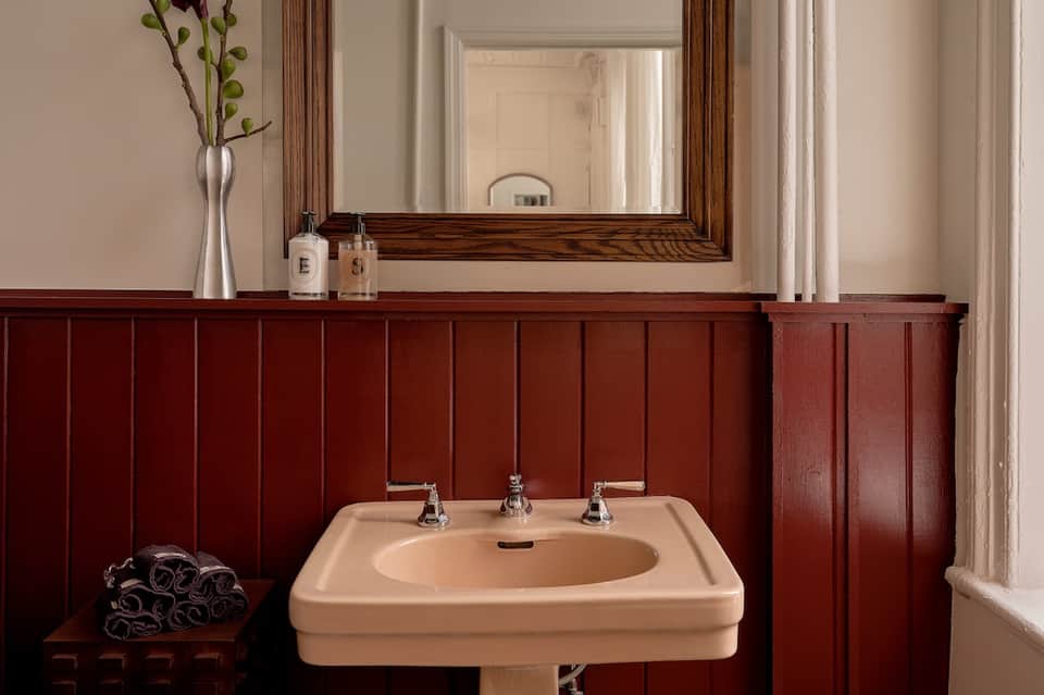 Elegant bathroom with pedestal sink, dark wood paneling, and large framed mirror