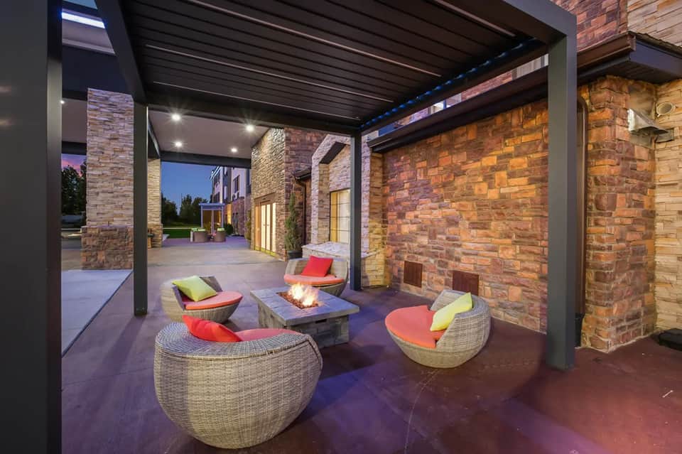 Modern outdoor lounge area with woven rattan chairs, fire pit, brick walls, and integrated lighting at dusk