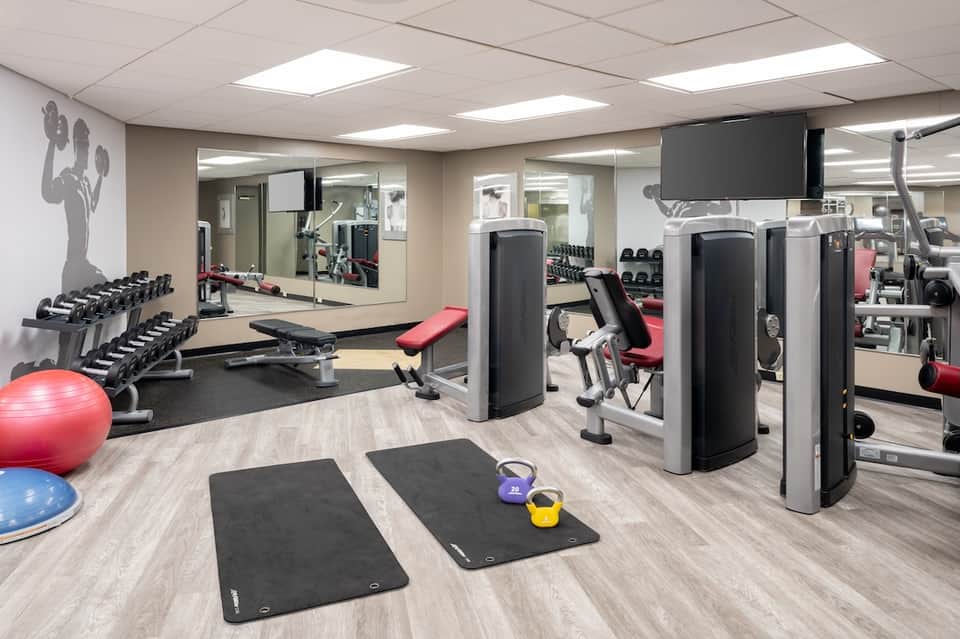 Fitness center with dumbbells, cardio equipment, exercise mats, stability balls, and mirrored walls