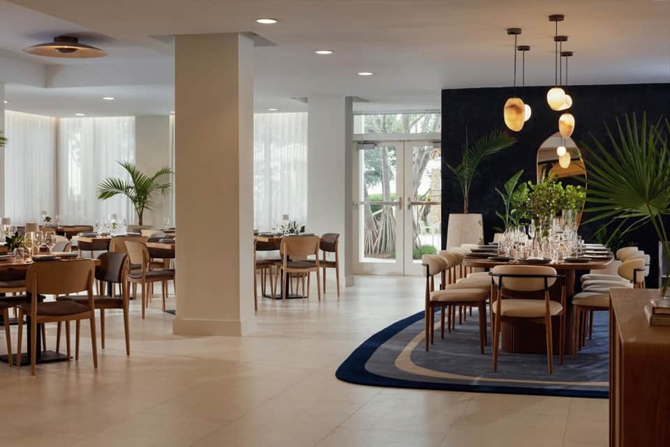 Contemporary dining room with wooden chairs, pendant lights, potted plants, and bright windows