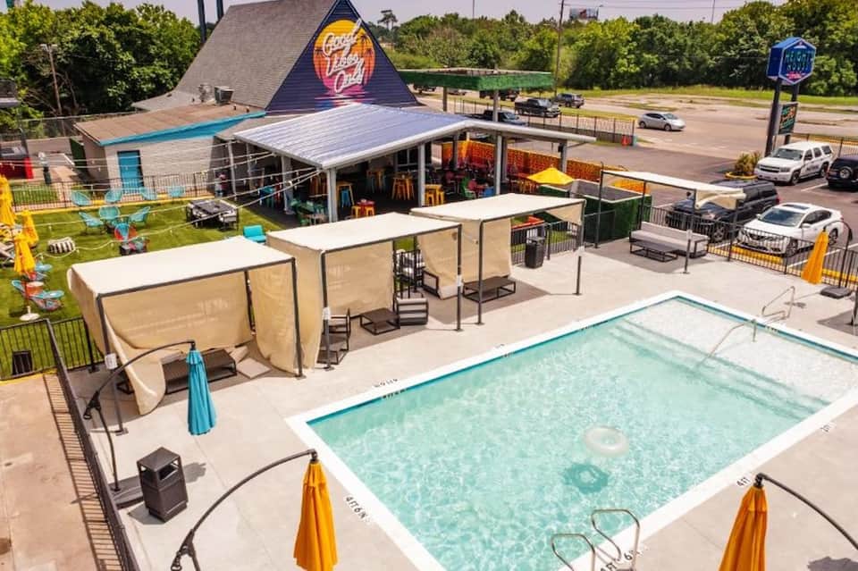 Modern poolside area with shade structures, neon bar sign, and rectangular swimming pool