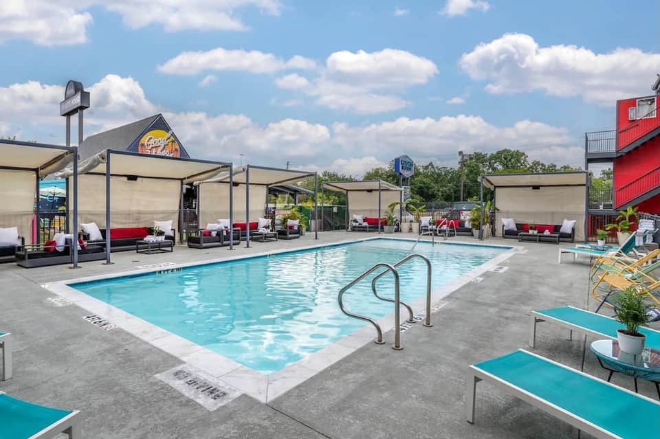 Resort pool with modern cabanas, shade structures, and red and white lounge seating areas