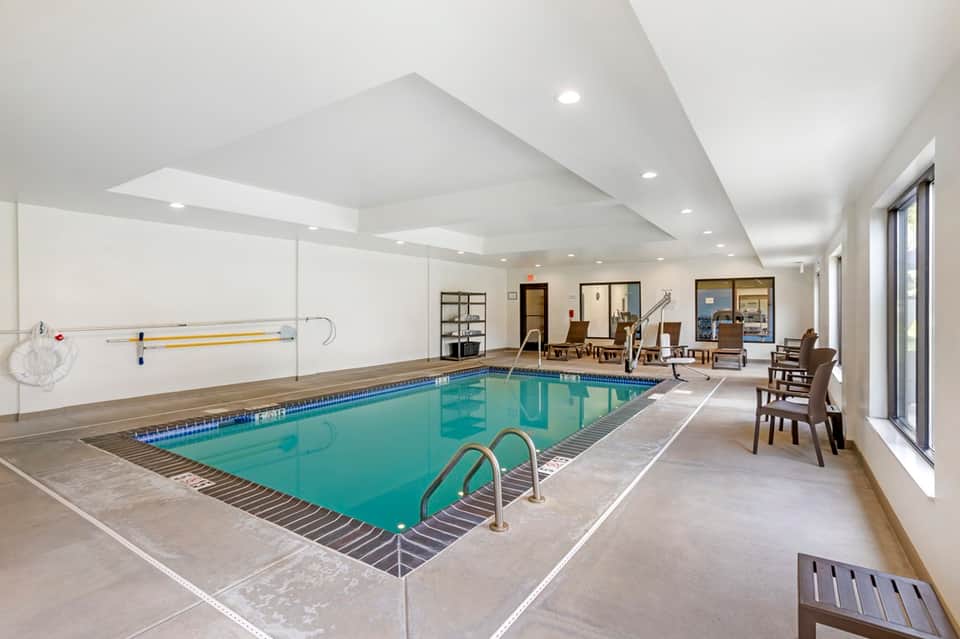 Indoor lap pool facility with bright ceiling, lounge seating, and glass doors leading to common areas