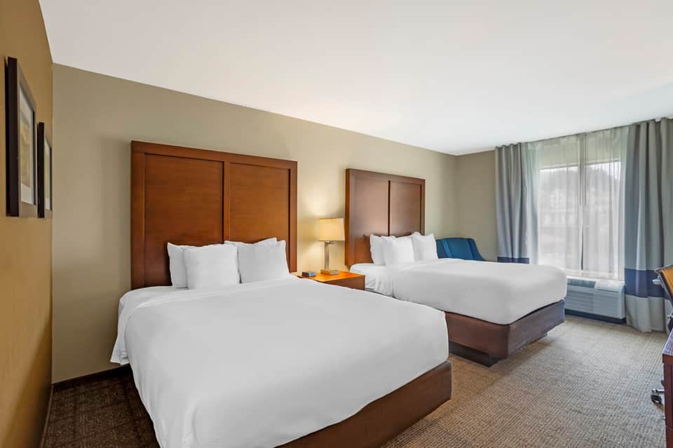 Double queen hotel room with wood headboards, warm lighting, and contemporary furnishings