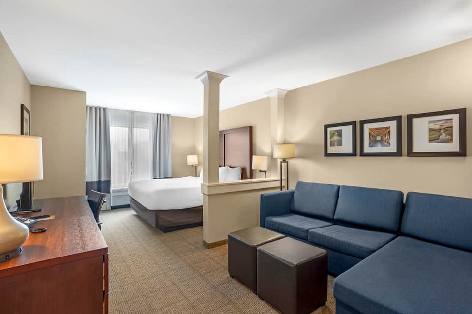 Hotel suite with king bed, blue sofa, desk, and neutral color palette