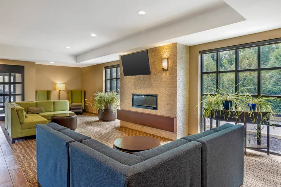 Contemporary lobby lounge with blue seating, stone fireplace, large windows, plants, and warm lighting