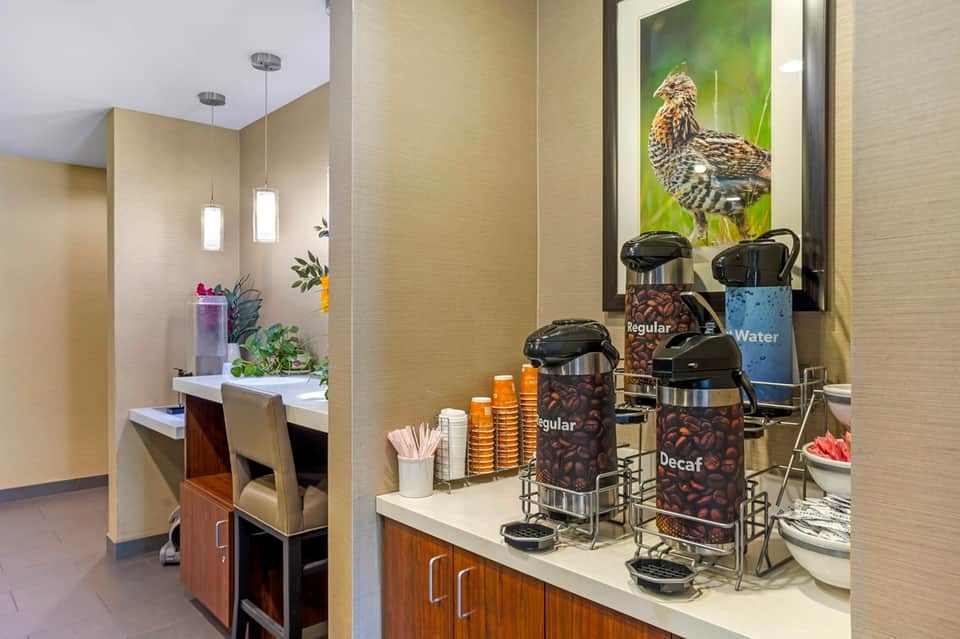 Hotel coffee station with labeled dispensers, supplies, and bird artwork on wall