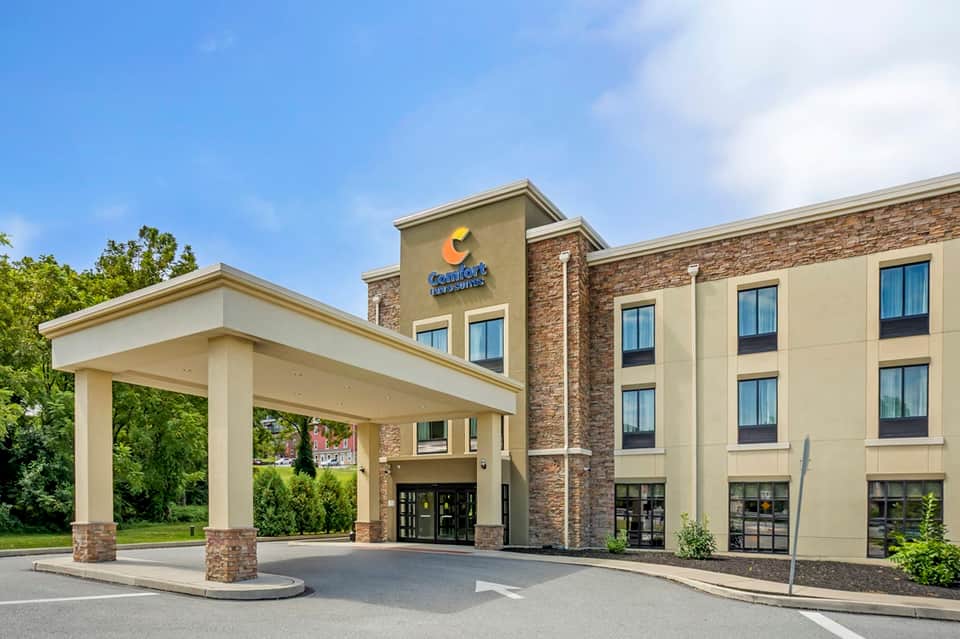 Exterior of mid-rise hotel with stone and tan facade, entrance awning, and surrounding greenery