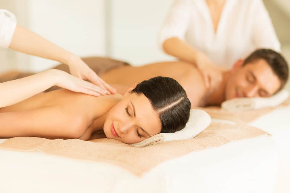 Couple receiving back massage treatment at spa on sand-colored table