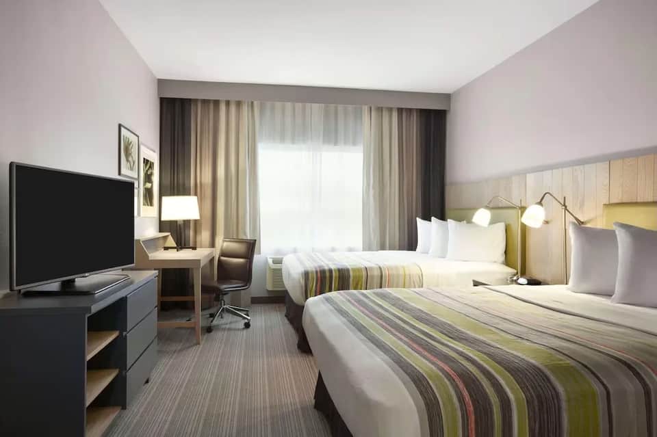 Hotel room with two queen beds, striped bedding, work desk, and warm neutral color scheme