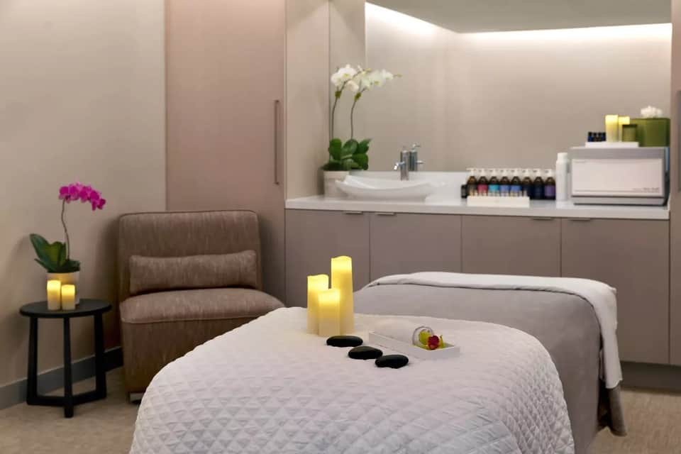 Spa treatment room with massage table, sink area, flowers, and ambient lighting