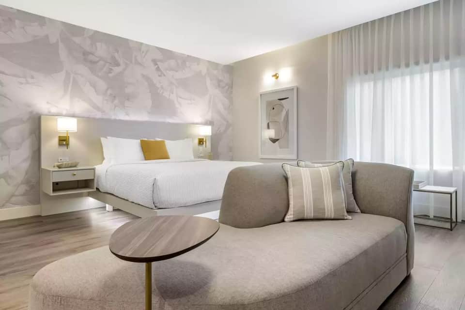 Modern hotel suite with king bed, seating area, and neutral contemporary design