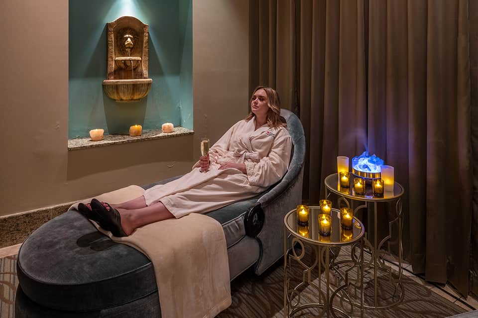 Woman relaxing in spa relaxation room with golden water fountain and candlelit tables