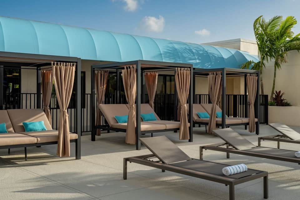 Modern spa deck with cabana beds, turquoise canopy, beige cushions, and tropical plants