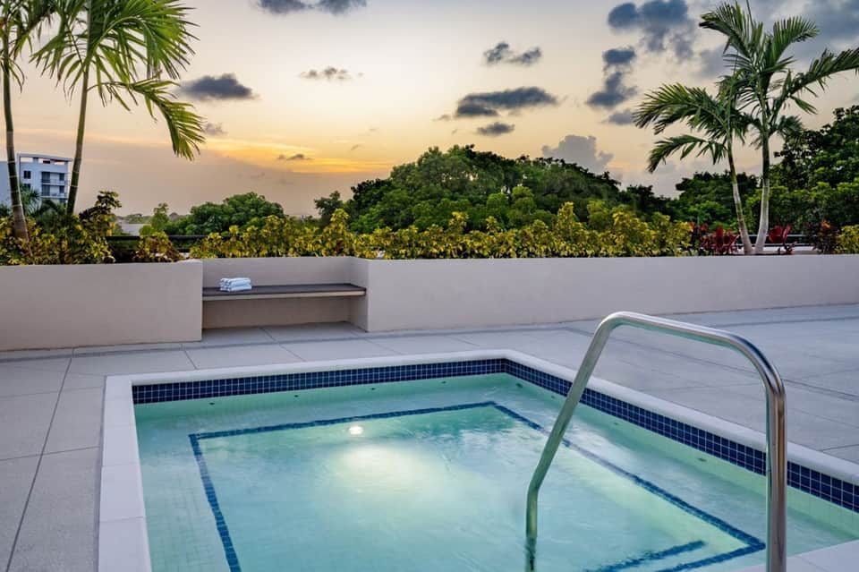 Rooftop plunge pool at dusk with palm trees, white walls, tropical landscape view, and sunset sky