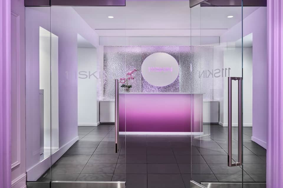 Minimalist pink neon spa reception with glass doors, white walls, and illuminated circular logo