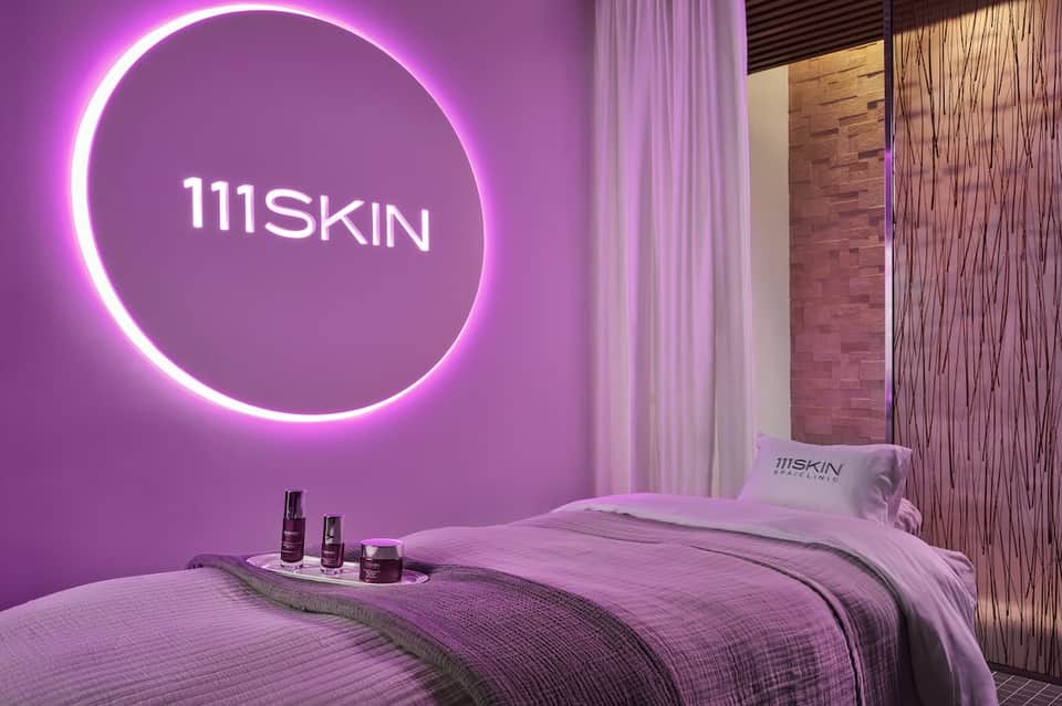 Luxurious spa treatment room with neon pink circular light fixture above massage bed