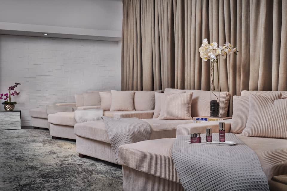 Luxury spa lounge with cream-colored ribbed seating, neutral curtains, white brick wall, and elegant furnishings