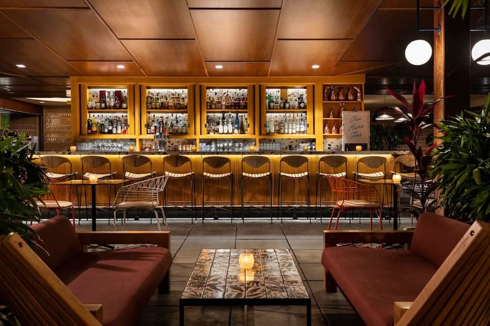 Upscale bar lounge with wooden accents, illuminated bottle display, and burgundy seating