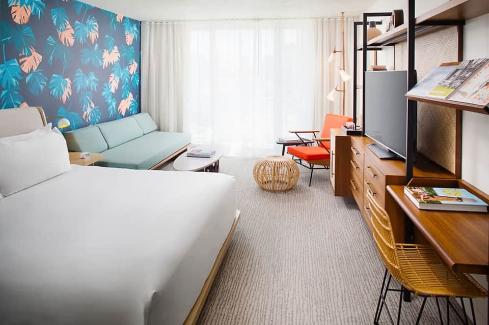 Modern hotel suite with king bed, turquoise palm wallpaper, sofa, and contemporary furnishings