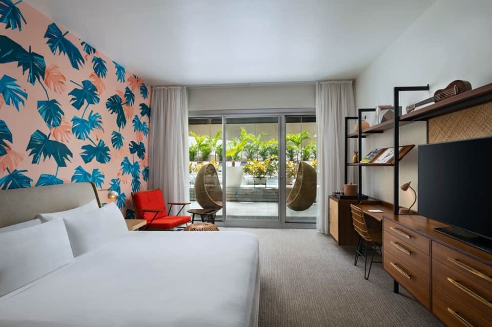 Bright hotel room with tropical leaf wallpaper, balcony access, and hanging chairs