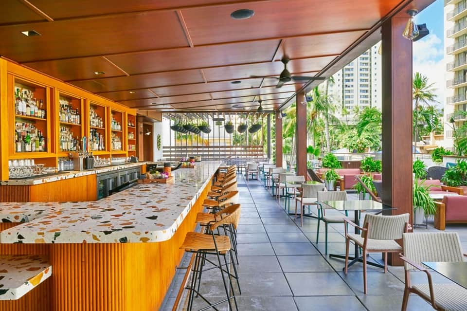 Open-air bar with wooden cabinetry, terrazzo counters, and tropical garden patio seating