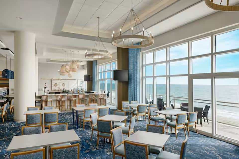 Upscale beachfront restaurant and bar with floor-to-ceiling windows, ocean view, and pendant lighting