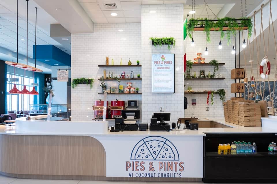 Bright café counter at Pies & Pints with white subway tile, floating shelves, and hanging plants