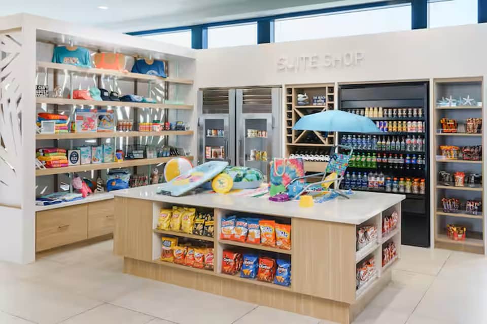 Bright retail shop interior with wooden shelving, colorful beach toys, snacks, and beverages