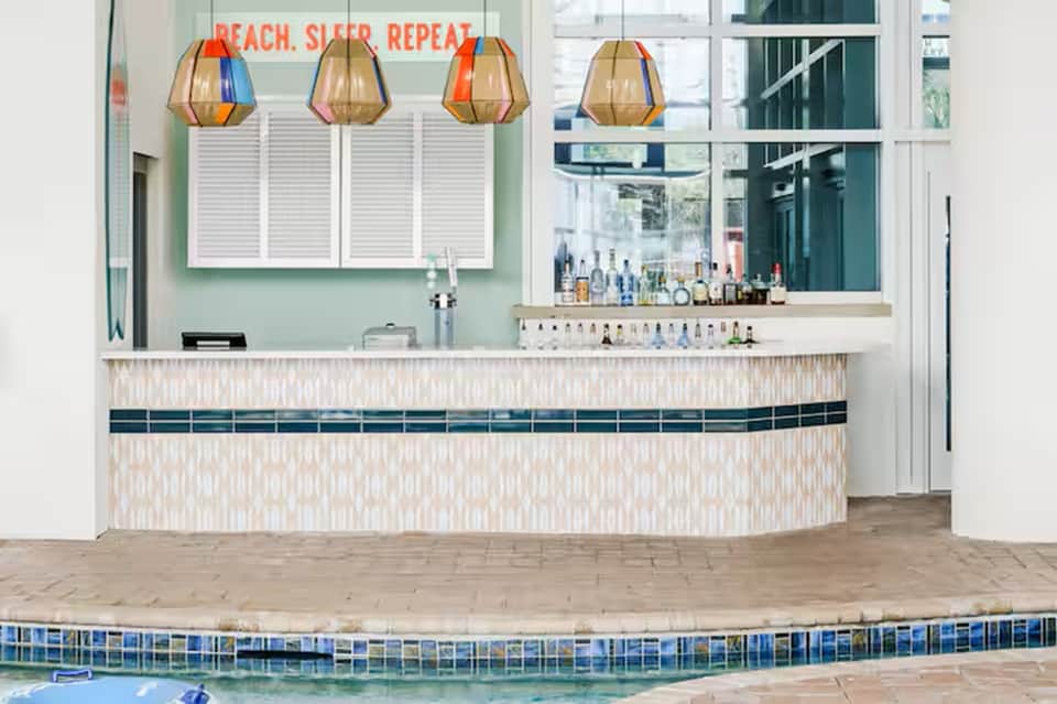 Pool bar with geometric pendant lights, turquoise wall, tiled counter, and pool edge view