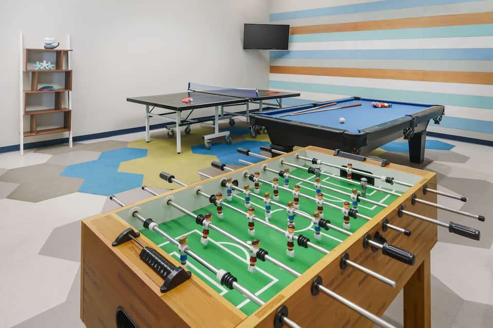 Game room with foosball table, pool table, ping pong table, and colorful accent wall