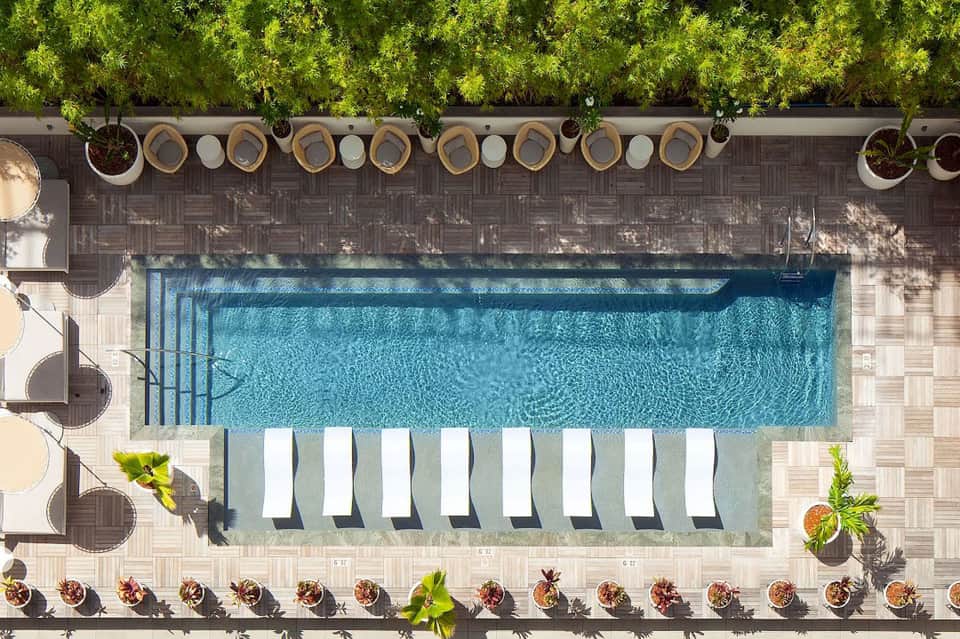 Aerial view of lap pool with lounge chairs, tropical landscaping, and woven shade structures along edge