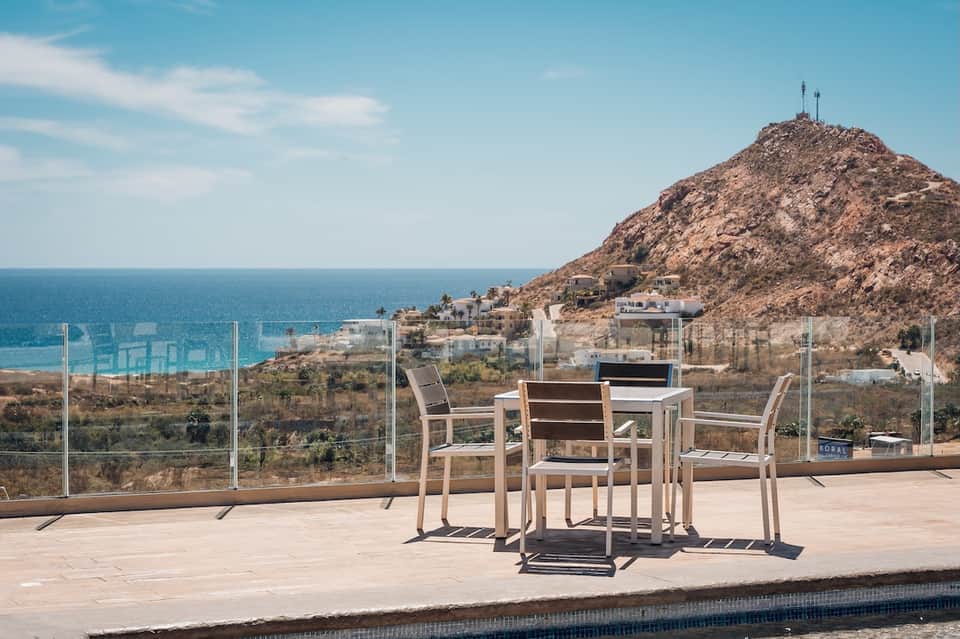 Beachfront terrace with dining table overlooking ocean, rocky coastline, and Mediterranean village