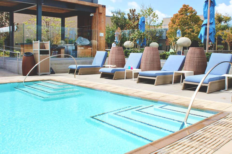 Contemporary pool area with woven loungers, blue cushions, and spa pods overlooking manicured grounds