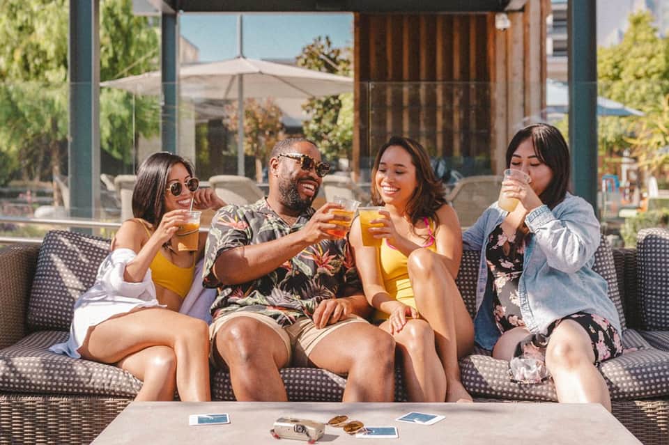 Group of four friends toasting with drinks on outdoor patio seating area during daytime